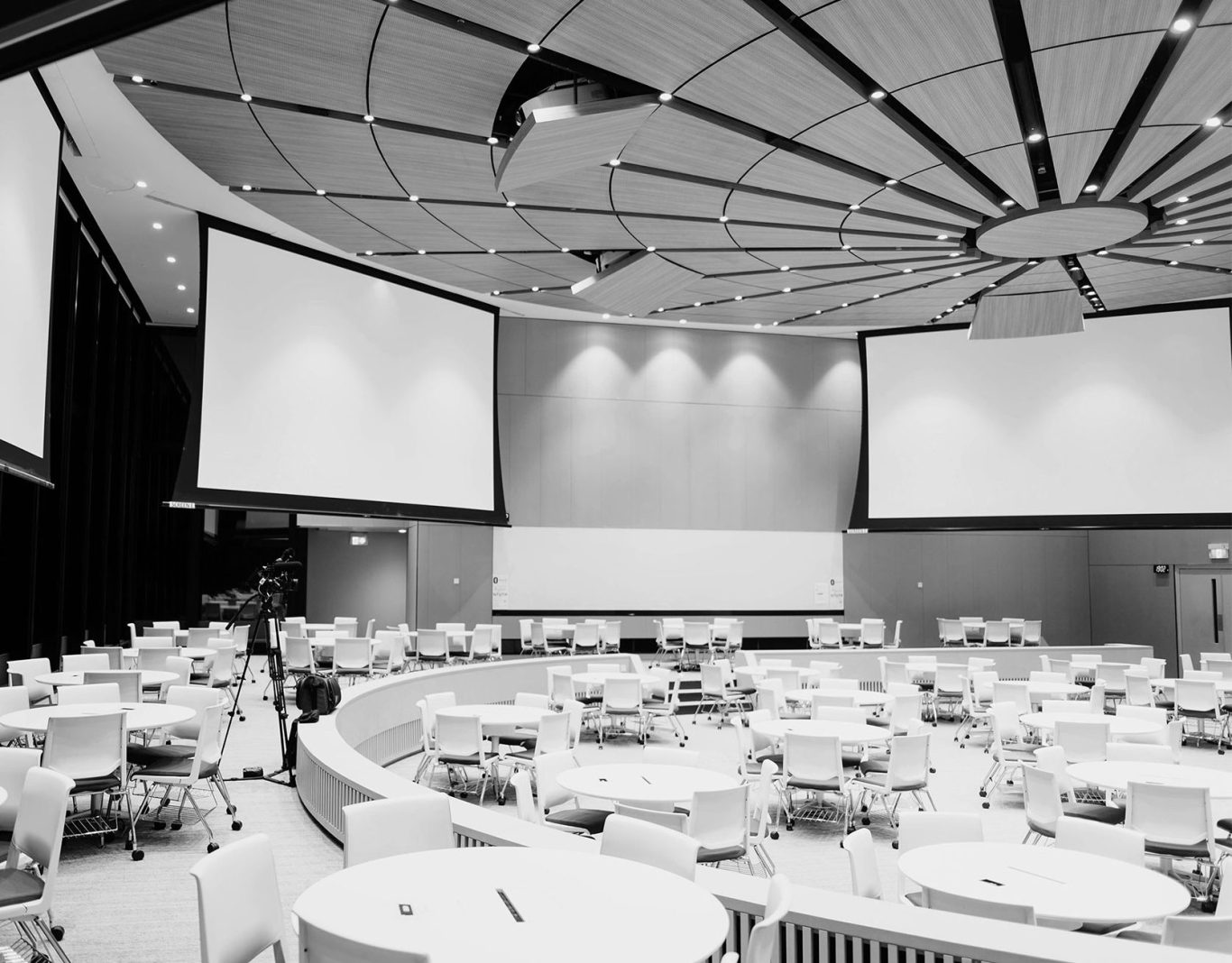 Sala de conferencias con mesas redondas y pantallas grandes en las paredes.